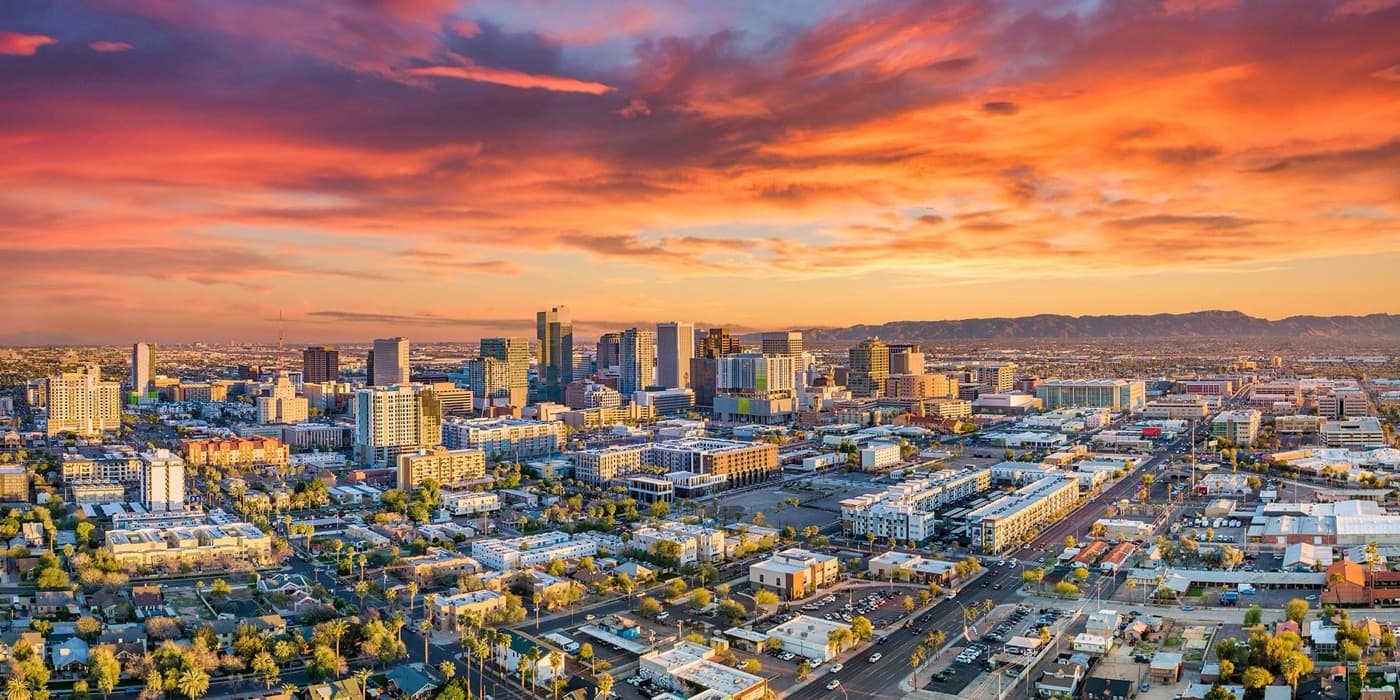 Aerial sunset view of downtown Phoenix, Arizona skyline with the city's towers glowing under a dramatic orange and pink sky